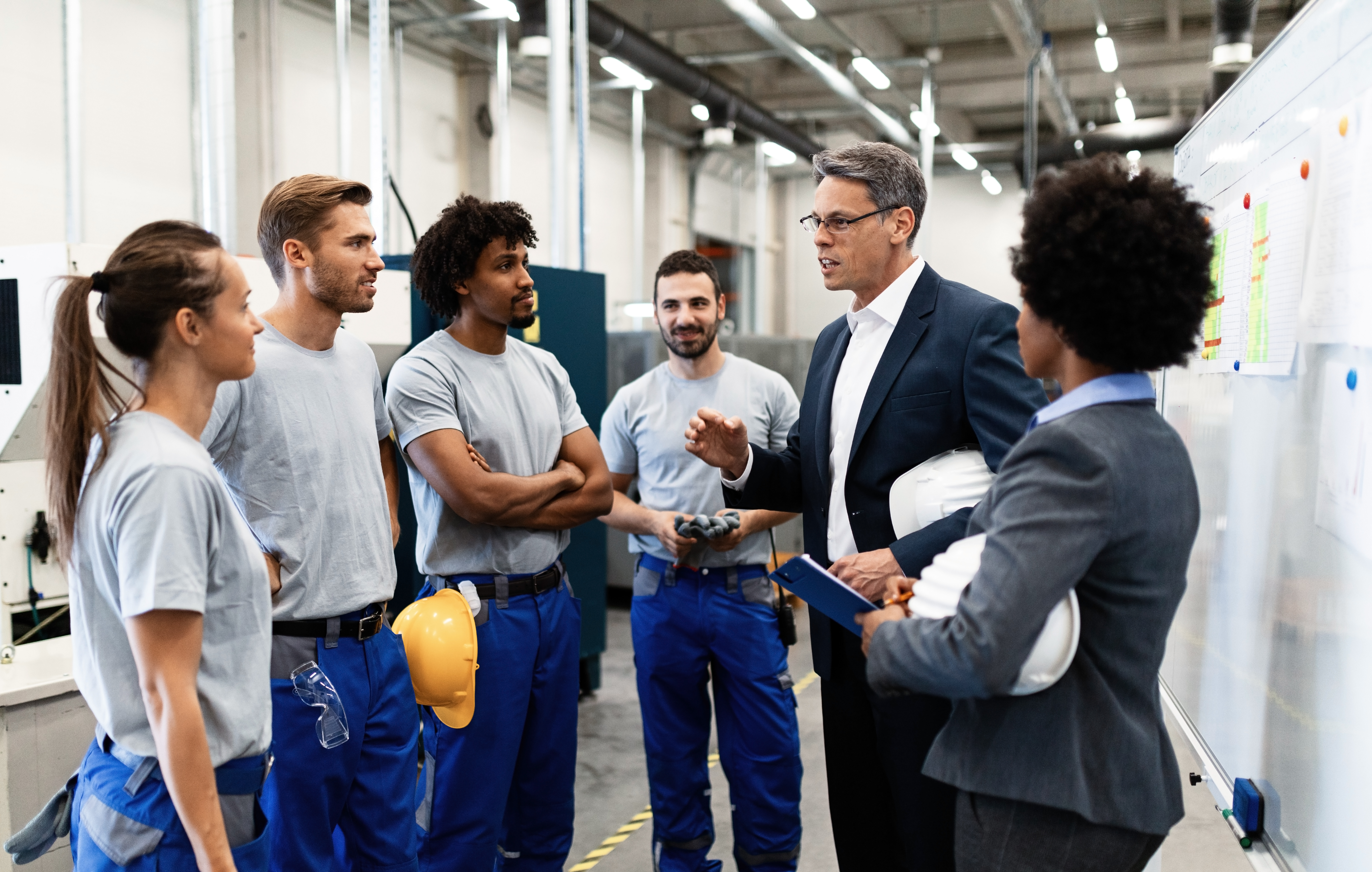 corporate manager talking group manual workers while having staff meeting factory